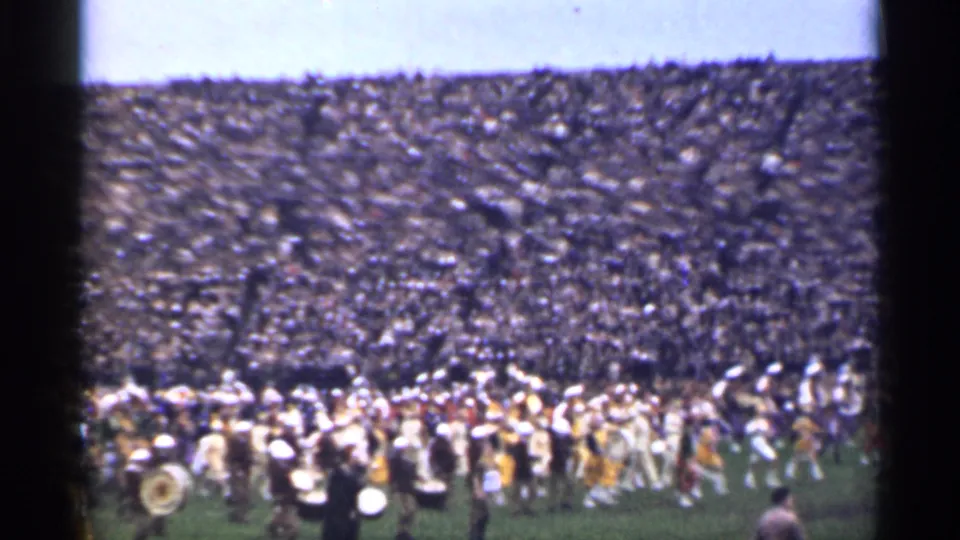 Home-movie view of a uniformed marching band performing on a stadium field in San Francisco, with a crowded audience in the stands.