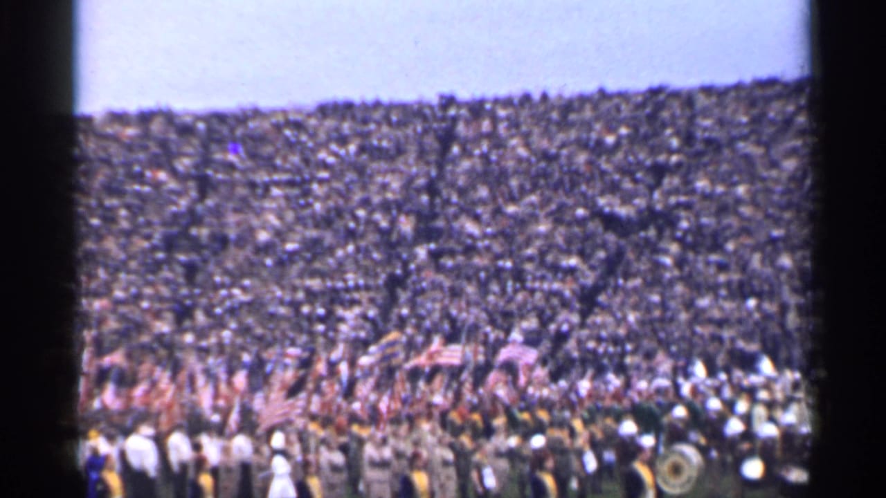 Packed San Francisco stadium scene with flag bearers and band members on the field in 1944 home-movie footage.