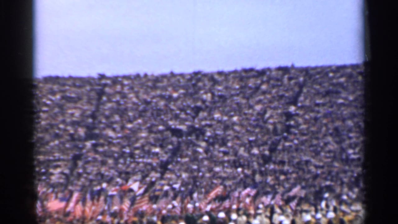 Distant 1944 San Francisco view of a dense outdoor crowd holding many American flags under a pale sky.