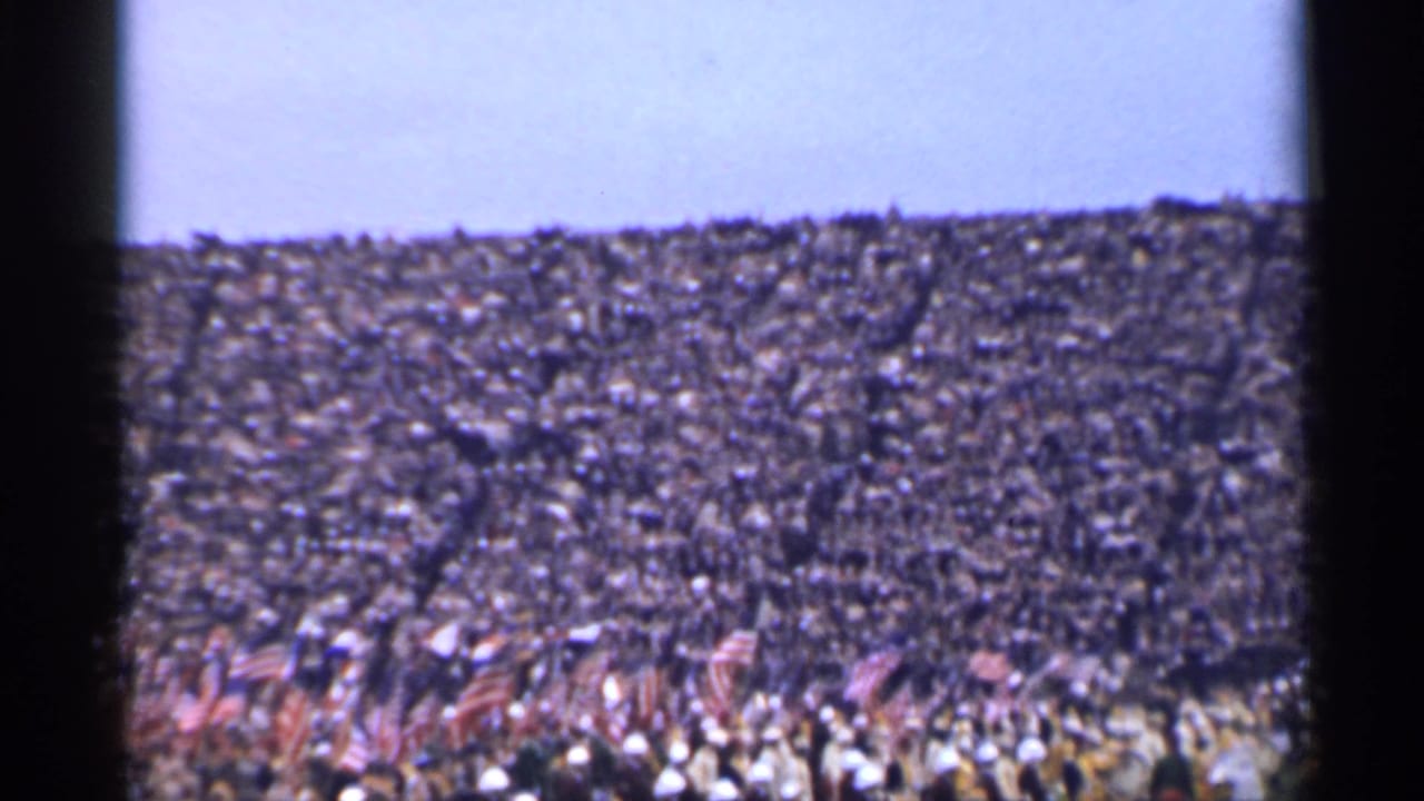 Dense crowd fills the frame with clusters of American flags near the foreground.