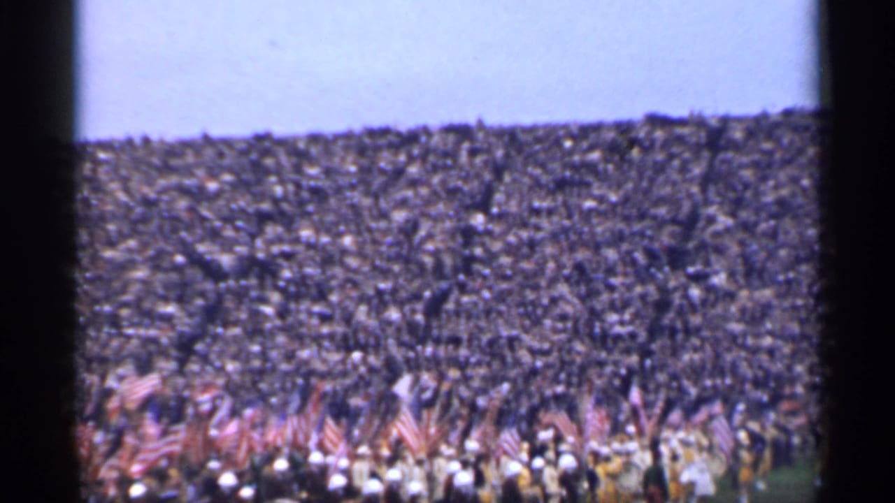1944 San Francisco home-movie frame showing a dense stadium crowd behind a foreground group carrying American flags.