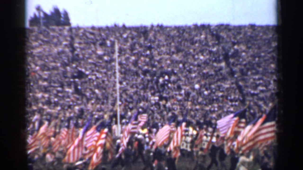 The 1944 San Francisco ceremony continues with multiple American flags in the foreground and a packed grandstand beyond.