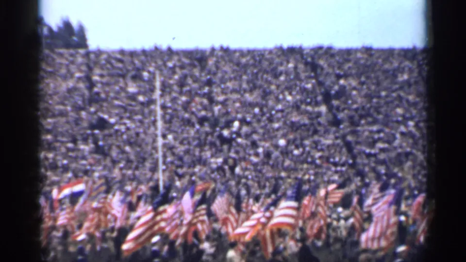 1944 San Francisco stadium scene with dense spectators and American flags waving near the camera.