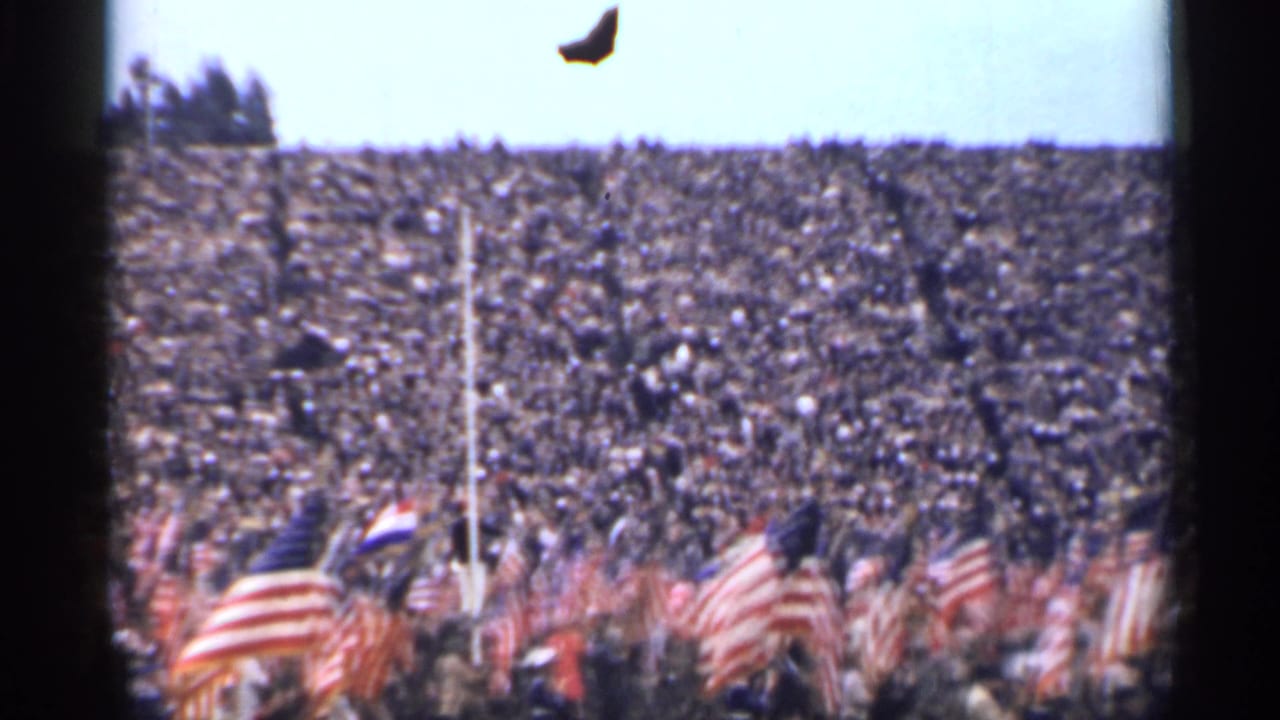 1944 San Francisco home-movie frame showing packed stands, flags, and a flagpole during a public gathering.