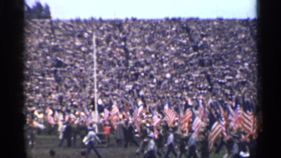 1944 San Francisco home-movie view of a patriotic stadium crowd with flags and moving figures in front.