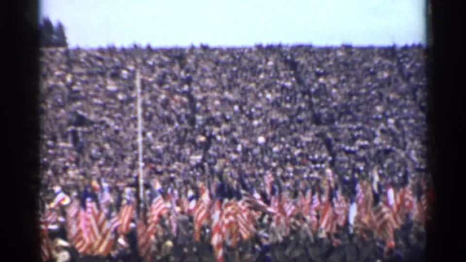 San Francisco 1944 home-movie frame showing a patriotic flag procession moving past a full stadium audience.