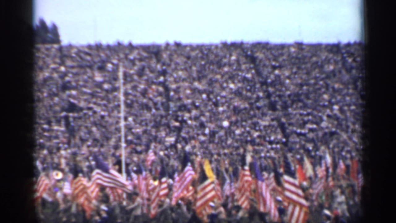 A 1944 San Francisco stadium scene with dense spectators and numerous American flags moving across the lower frame.