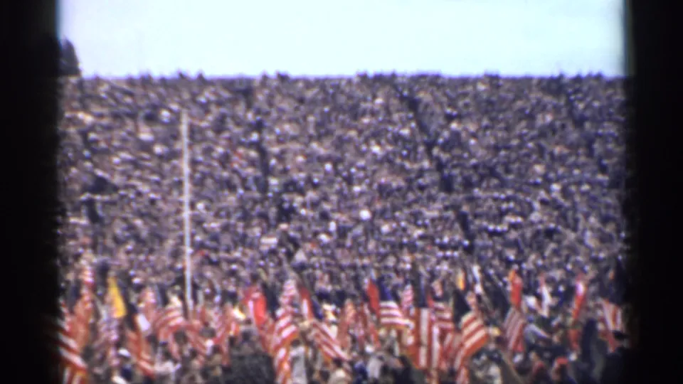 1944 San Francisco home-movie frame showing packed stadium stands and American flags near the field during a public ceremony.