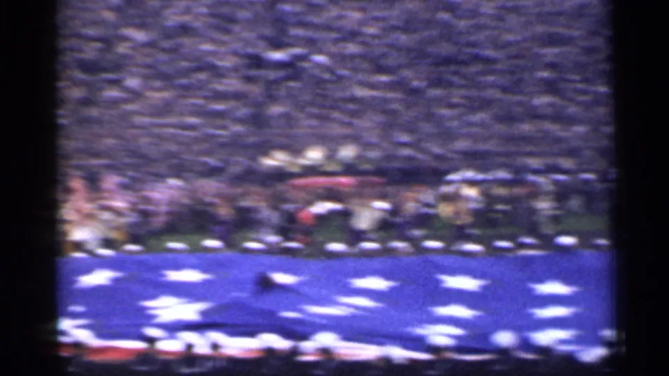 Soft 8mm frame of the large U.S. flag display on a San Francisco stadium field, with uniformed personnel and packed stands visible.
