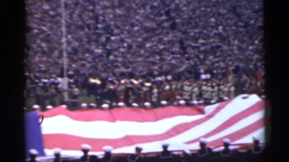 1944 San Francisco stadium ceremony frame with the striped portion of a large American flag in the foreground and military personnel nearby.