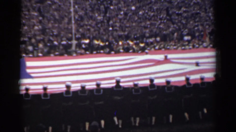1944 San Francisco frame showing a large U.S. flag across a stadium field with uniformed personnel in the foreground.