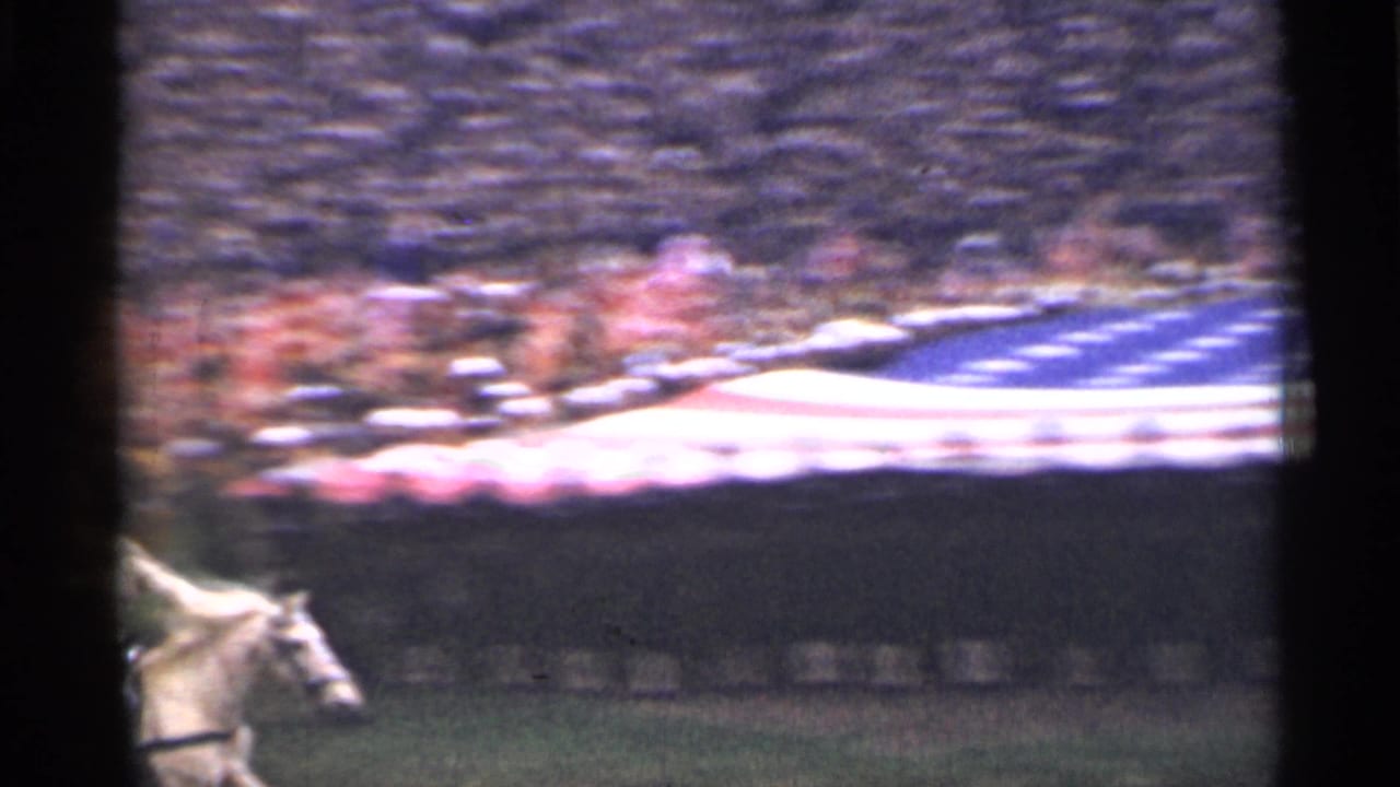 Large American flag spread across a field with a rider entering at the left.