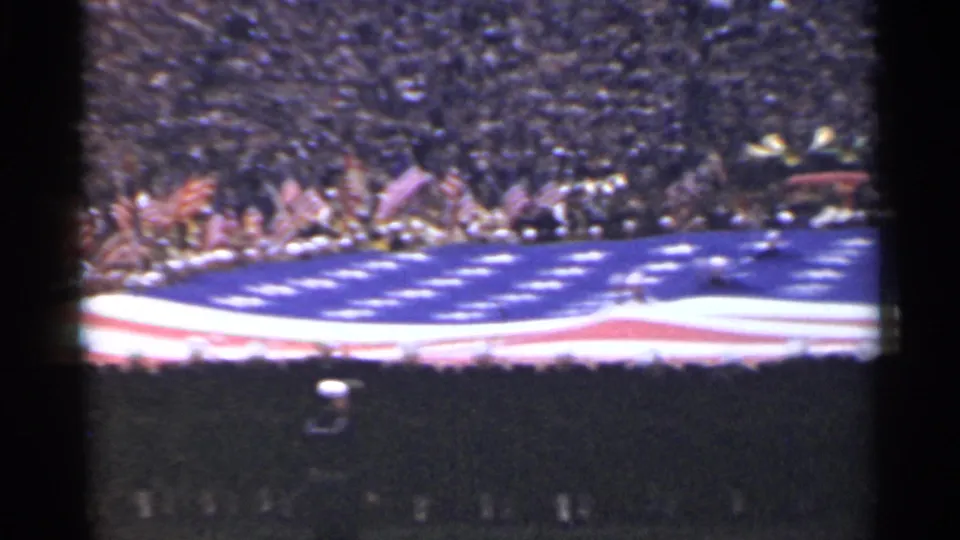1944 San Francisco home-movie frame showing spectators and a large U.S. flag unfurled across the ground.