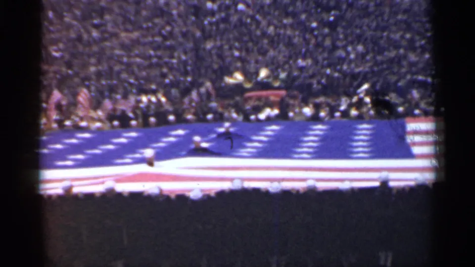 1944 San Francisco home-movie frame showing a huge American flag across a football field, with players and a dense crowd in the stands.