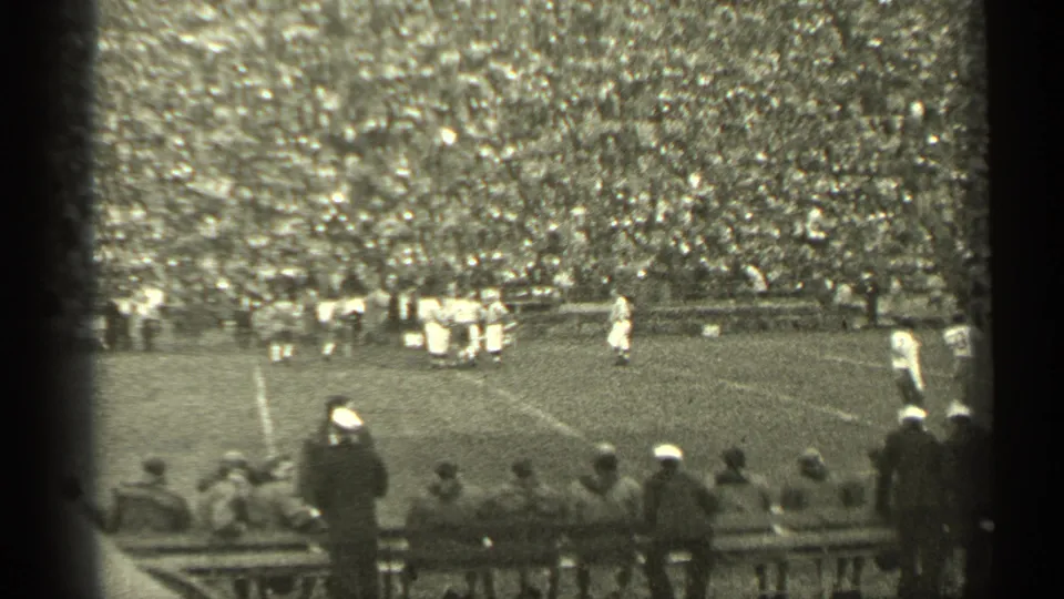 1944 San Francisco frame showing a wide football field view with players, sideline viewers, and a large crowd in the background.