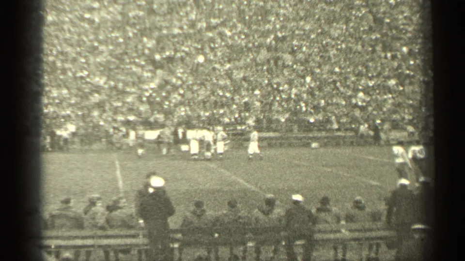 1944 San Francisco football footage showing players in white on the field, a dense crowd in the stands, and sideline spectators in hats.