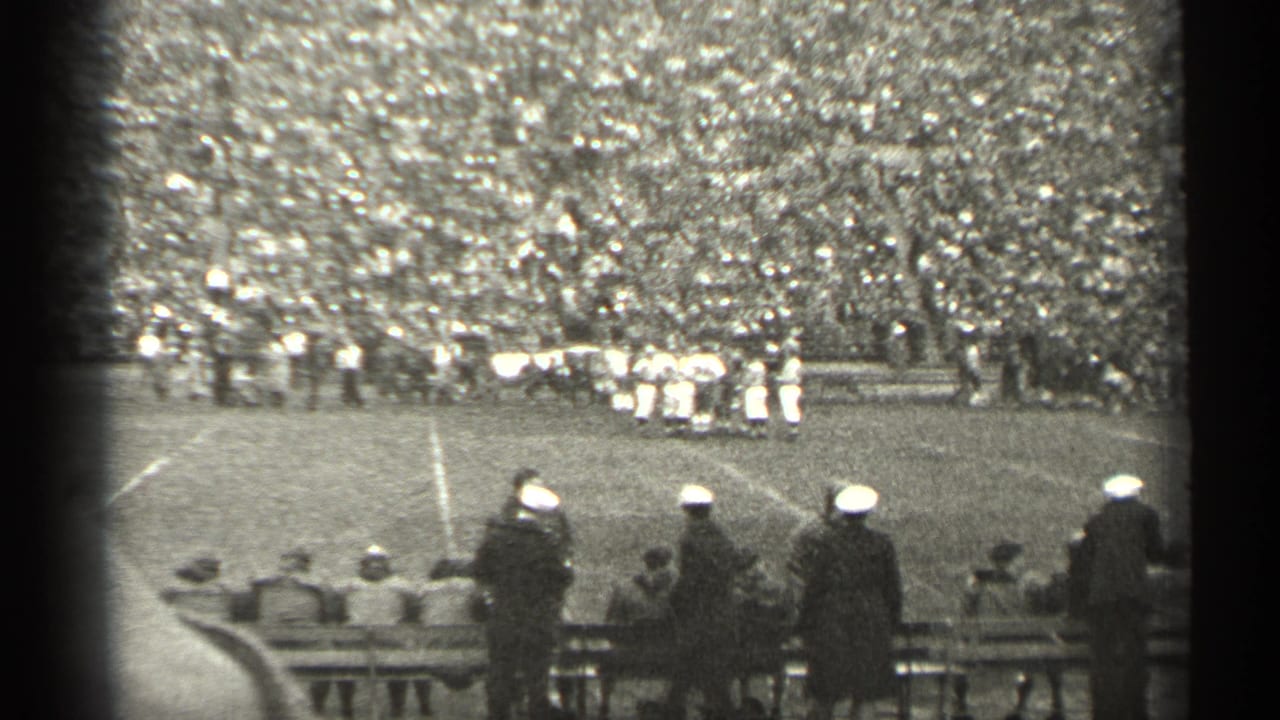 1944 San Francisco home-movie frame with spectators near benches watching football players on a crowded stadium field.