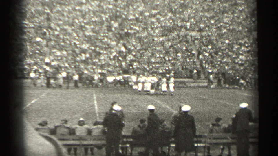 1944 San Francisco home-movie frame with spectators near benches watching football players on a crowded stadium field.
