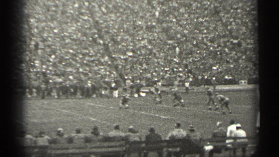 Players run across a San Francisco football field in this 1944 8mm frame, with spectators seated along the sideline.