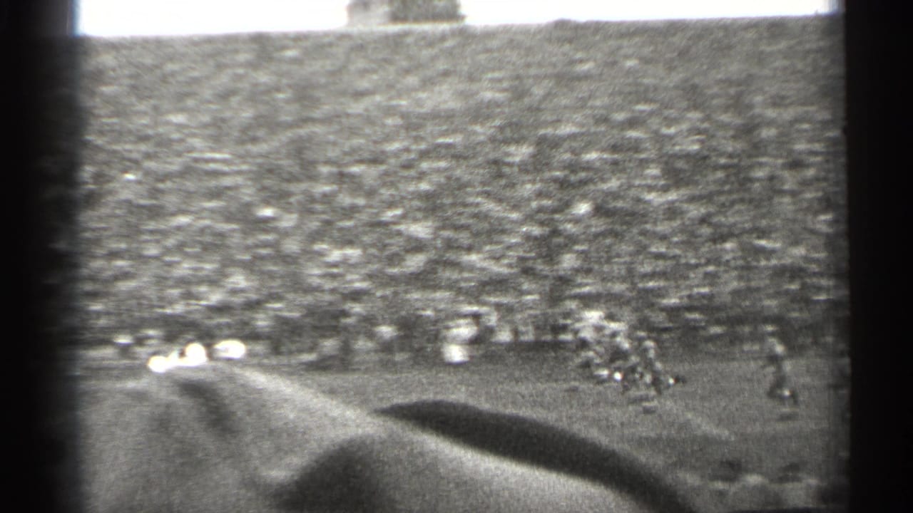 Crowded football stadium viewed from the stands with players on the field.