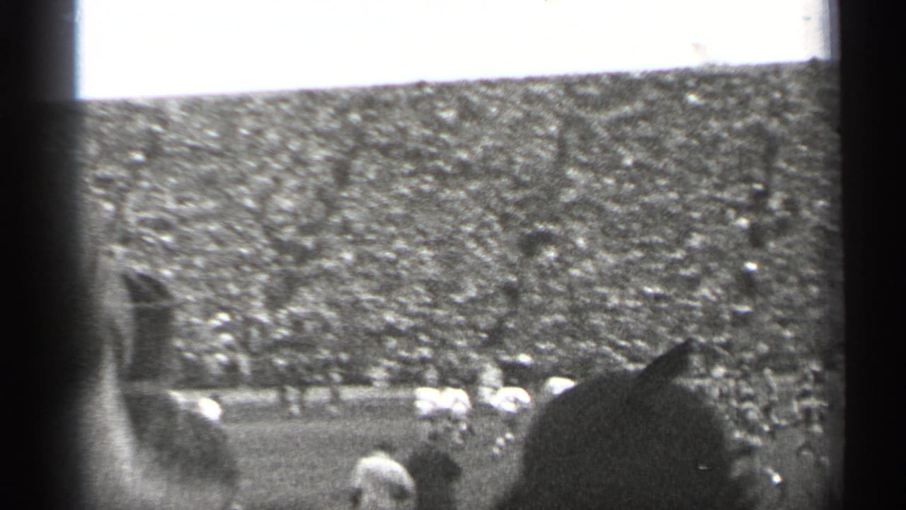 Football field and packed stands partly blocked by a foreground spectator.