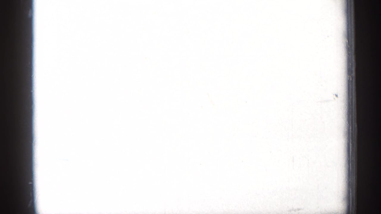 Mostly overexposed film leader or frame edge with a small stadium scene at lower left.