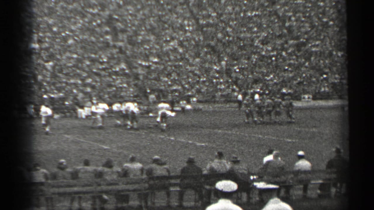 San Francisco 1940s home-movie view of a football game, with players spread across the field and a dense stadium crowd behind them.