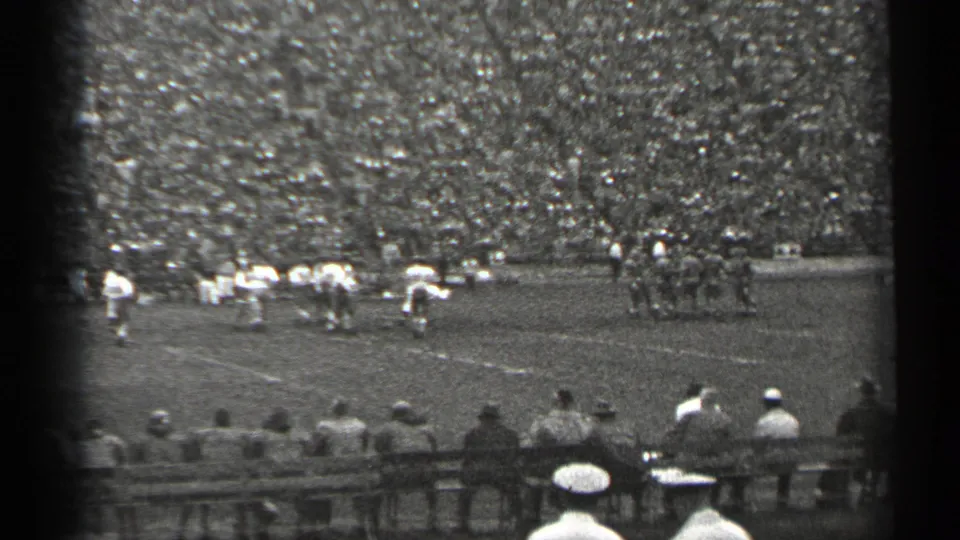 San Francisco 1940s home-movie view of a football game, with players spread across the field and a dense stadium crowd behind them.