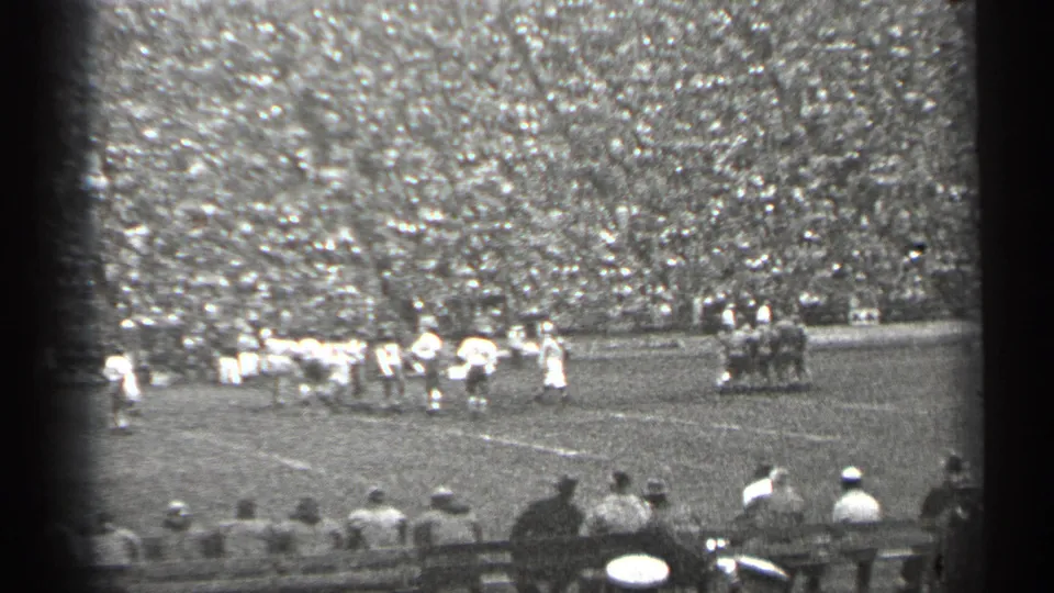 1940s San Francisco football scene with players forming near the line, a group in dark uniforms to the right, and spectators seated in front of crowded stands.