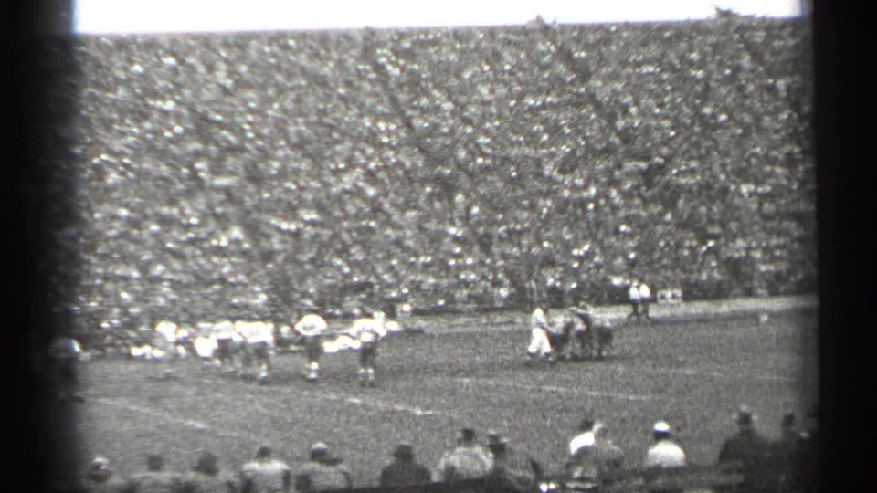 1944 San Francisco home-movie frame showing football players on the field with a dense crowd filling the stands behind them.