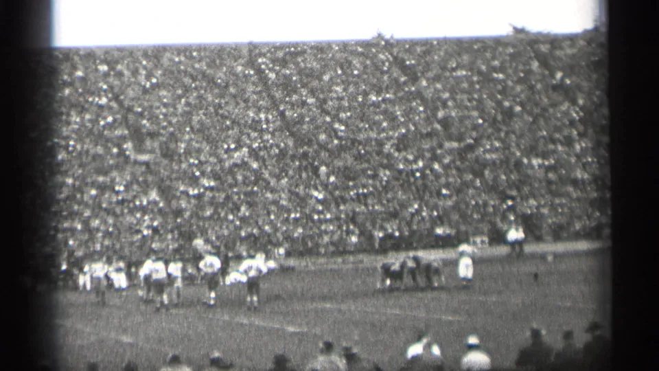 Grainy 1944 San Francisco stadium view with football players below crowded bleachers and spectators silhouetted in the foreground.