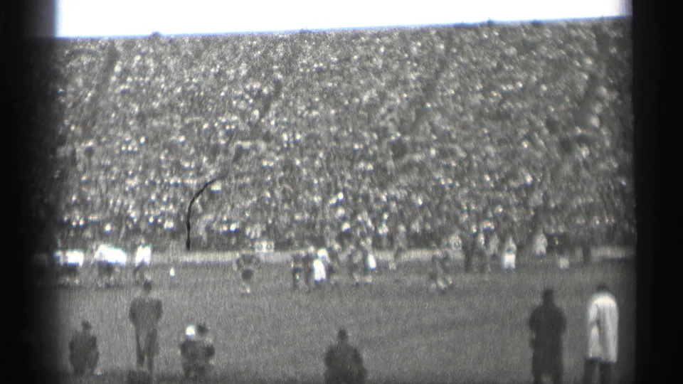 Black-and-white home-movie view of a San Francisco football game, showing sideline observers and a packed grandstand.