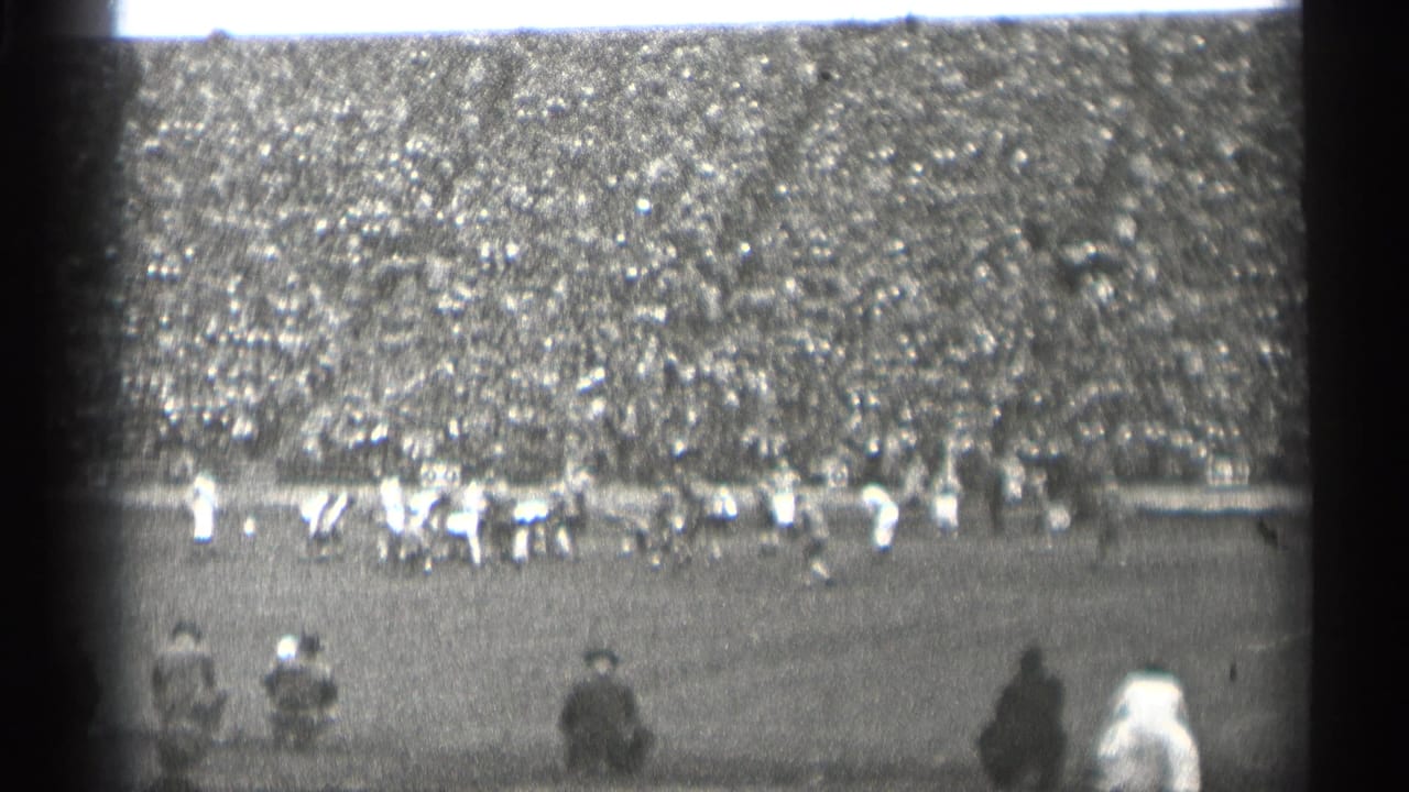 Distant football play in front of a packed stadium crowd.