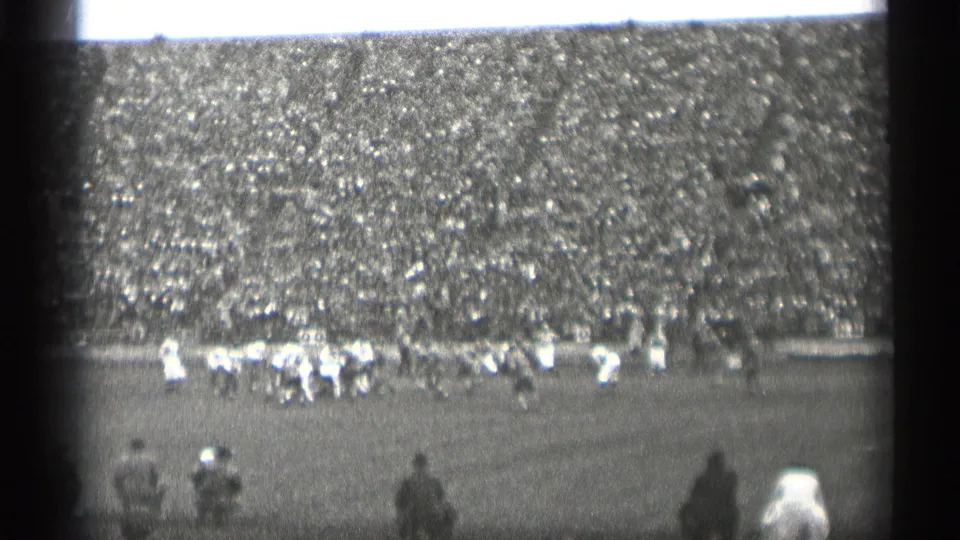 Distant 1944 San Francisco football action with light and dark uniforms visible below a densely packed stadium crowd.