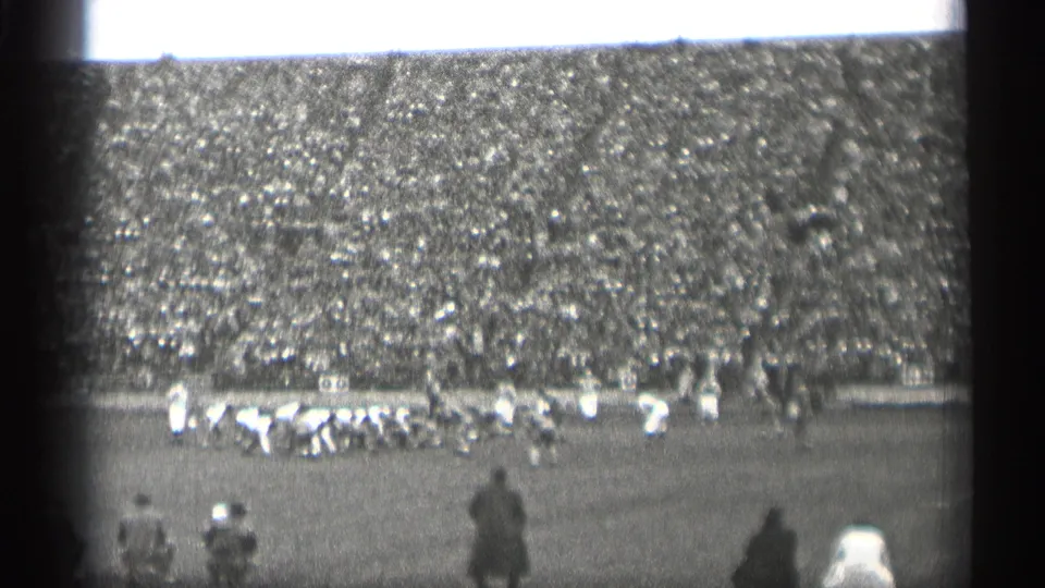 Home-movie frame of a football play or huddle in a packed San Francisco stadium, filmed from a distant spectator seat in 1944.