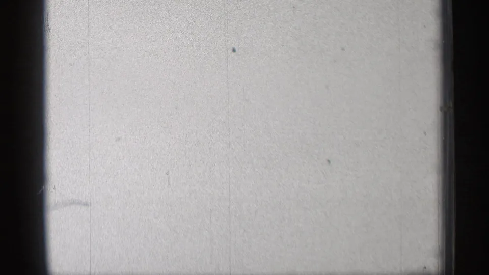Blank 8mm film leader or overexposed end frame with visible grain, faint vertical marks, and small dust specks.