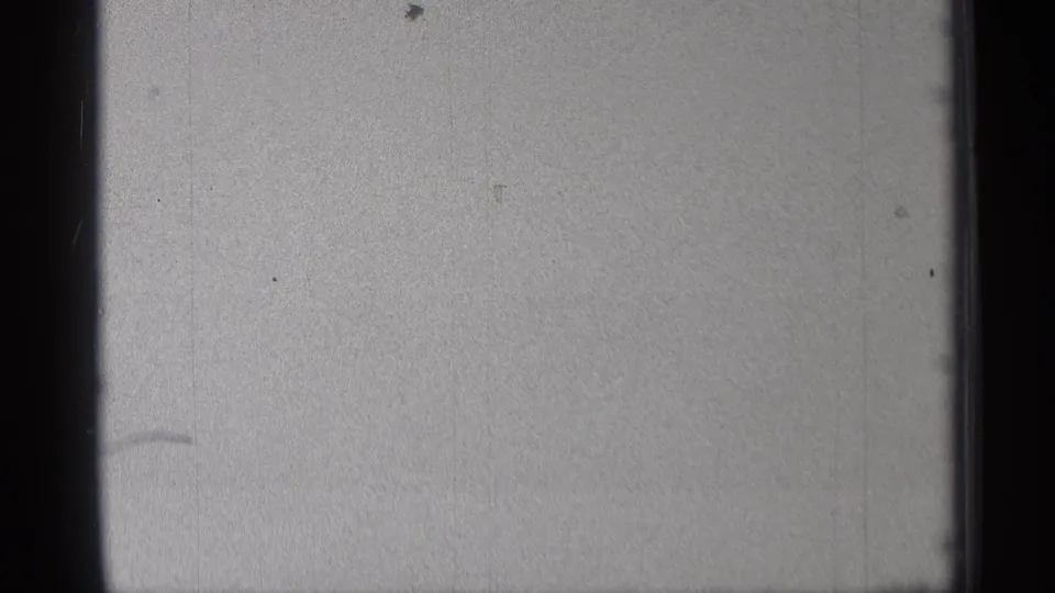 Mostly blank 8mm frame with gray exposure, dust specks, vertical marks, and dark film borders before the football scene begins.