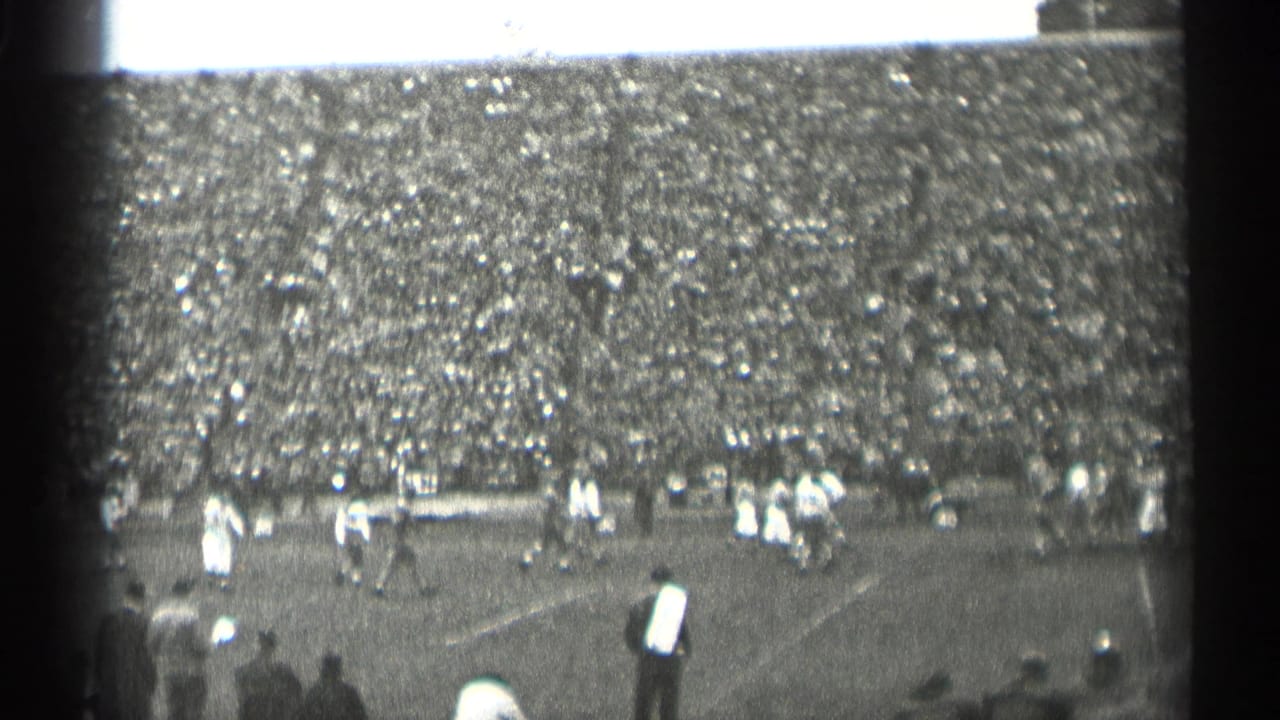 Football game seen from the stands with a packed crowd and players on the field.