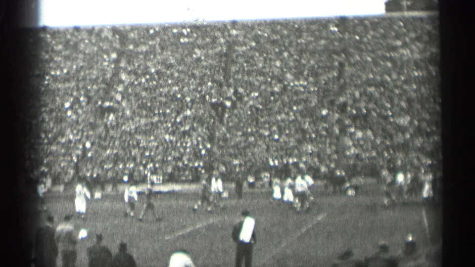 1944 San Francisco 8mm view of a football game, with players on the field, a striped official, and packed stadium seating behind them.