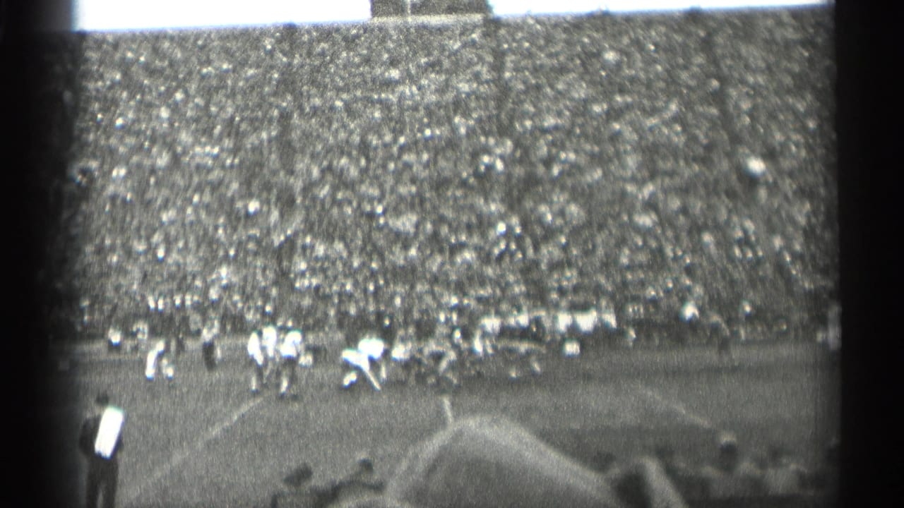 1944 San Francisco football footage showing a play forming on the field, with sideline figures and dense crowd seating in the background.