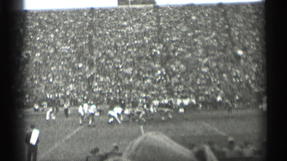 1944 San Francisco football footage showing a play forming on the field, with sideline figures and dense crowd seating in the background.