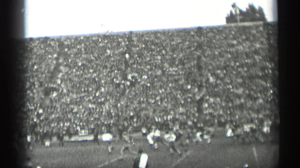 1944 San Francisco home-movie frame of a football field from the stands, with players at right and a large crowd filling the background.