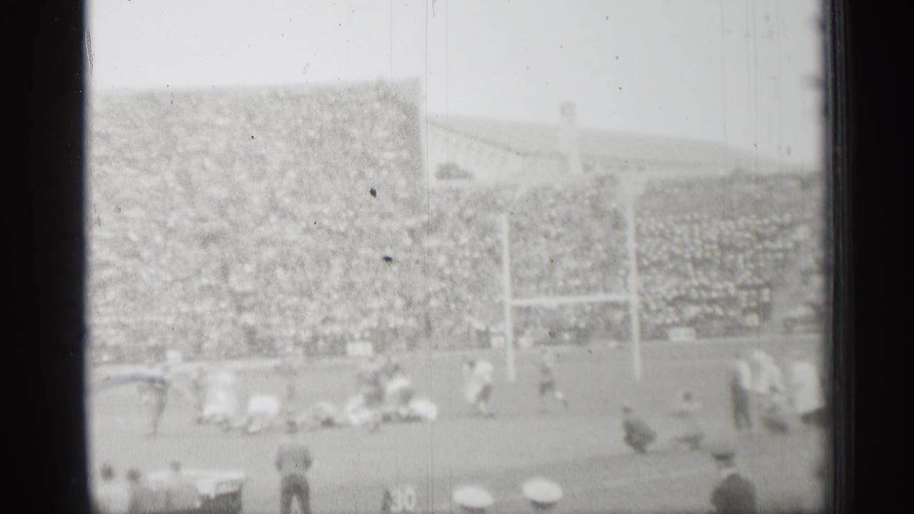 Distant football game in a packed stadium with goal posts and spectators.