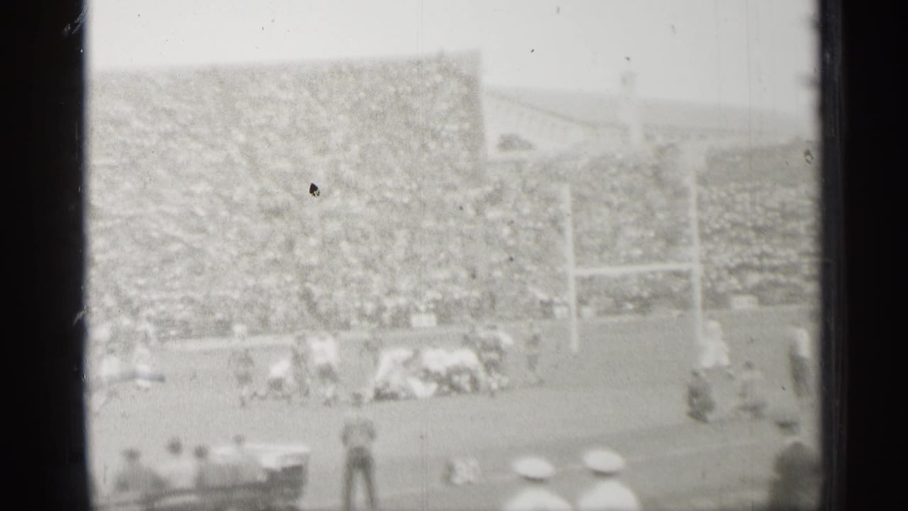 Distant 1944 San Francisco stadium view showing football players near the line, goal posts, dense crowd seating, and foreground spectators.