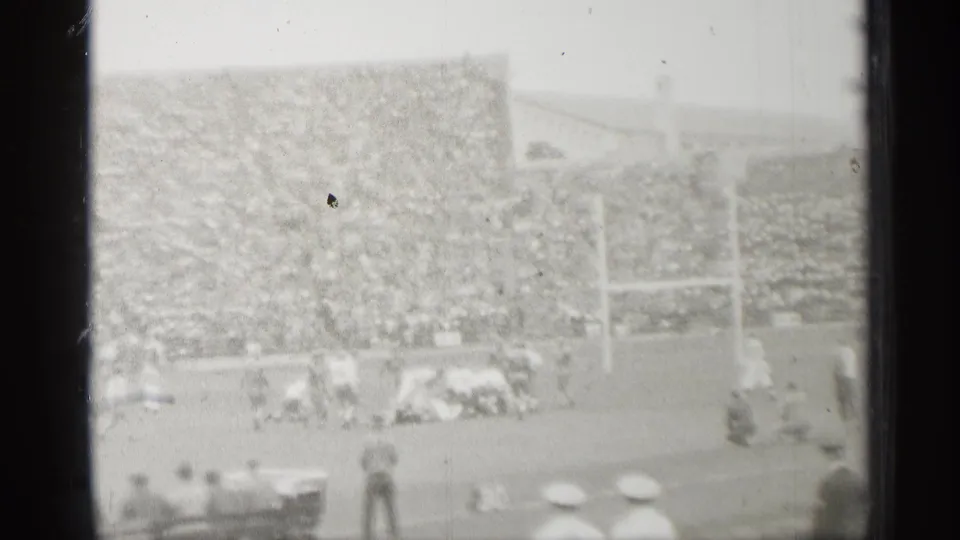 Distant 1944 San Francisco stadium view showing football players near the line, goal posts, dense crowd seating, and foreground spectators.