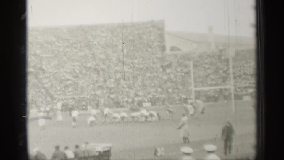 Home-movie football scene in San Francisco, 1944, with players spread across the field, a full grandstand, and spectators visible in the foreground.