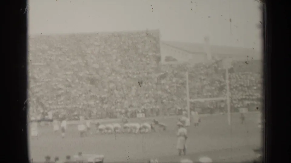 Distant 1944 San Francisco football view with players, goalposts, sideline figures, and dense spectators in the stands.
