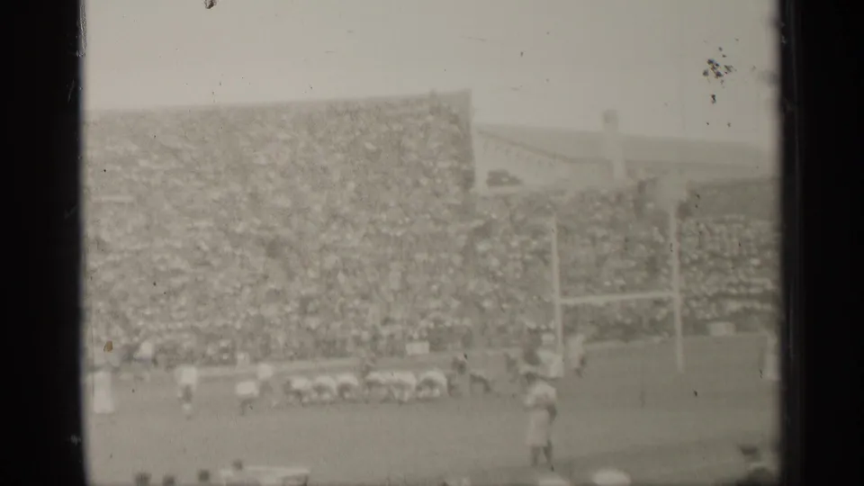 Wide 8mm frame of a San Francisco football game with players near the goalposts and spectators filling the background stands.