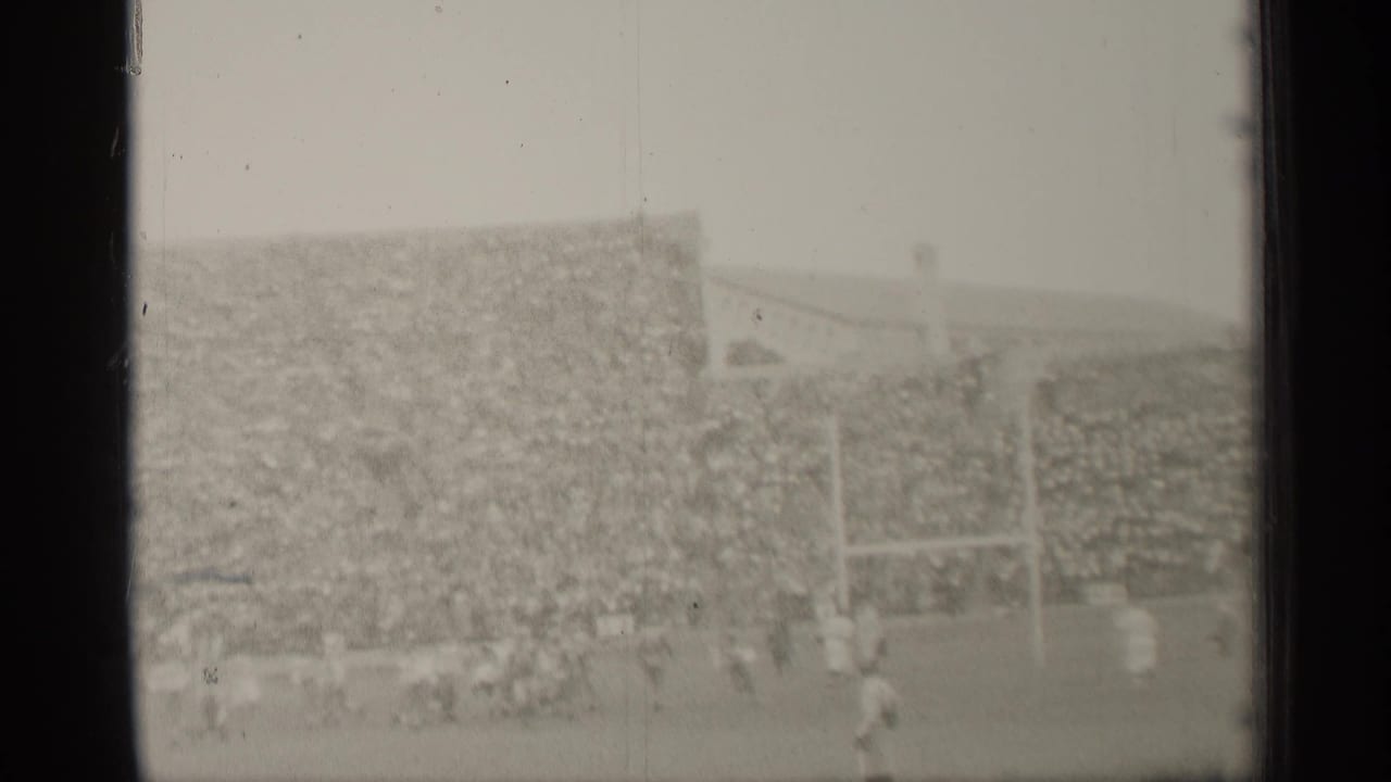 1944 San Francisco home-movie frame showing football players near goalposts before a densely filled stadium stand.