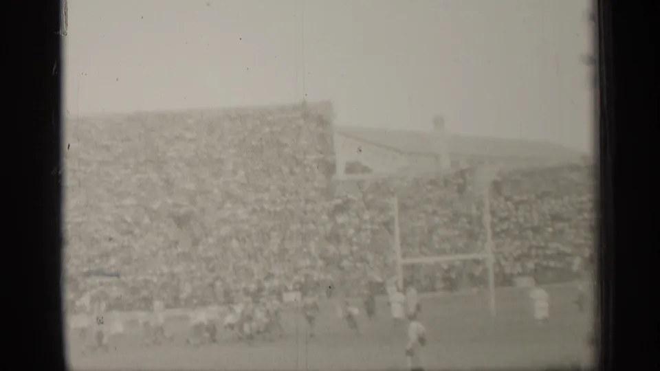 1944 San Francisco home-movie frame showing football players near goalposts before a densely filled stadium stand.